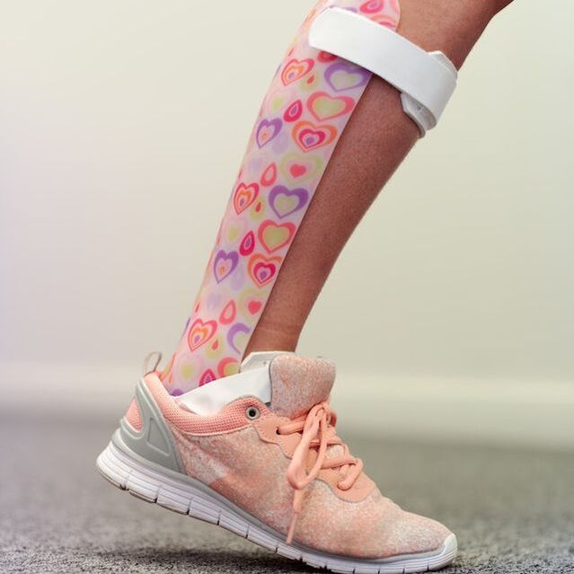 Person wearing a pink and white shoe with a heart-shaped brace on their leg